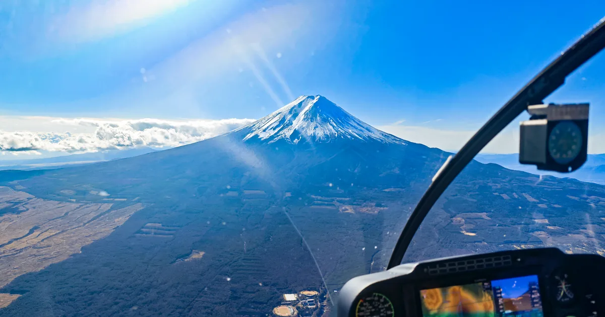 Snow-capped Mount Fuji seen through the windscreen of a helicopter, with the instrument panel in the foreground