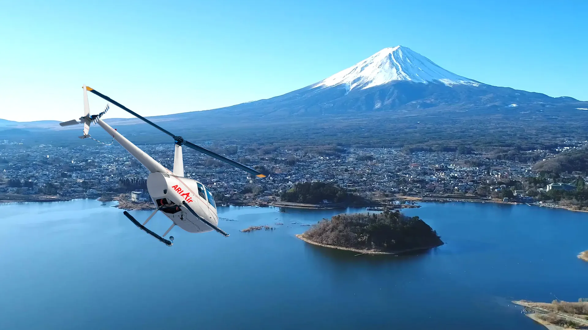 A small white helicopter over a lake below snow-capped Mount Fuji on a clear day