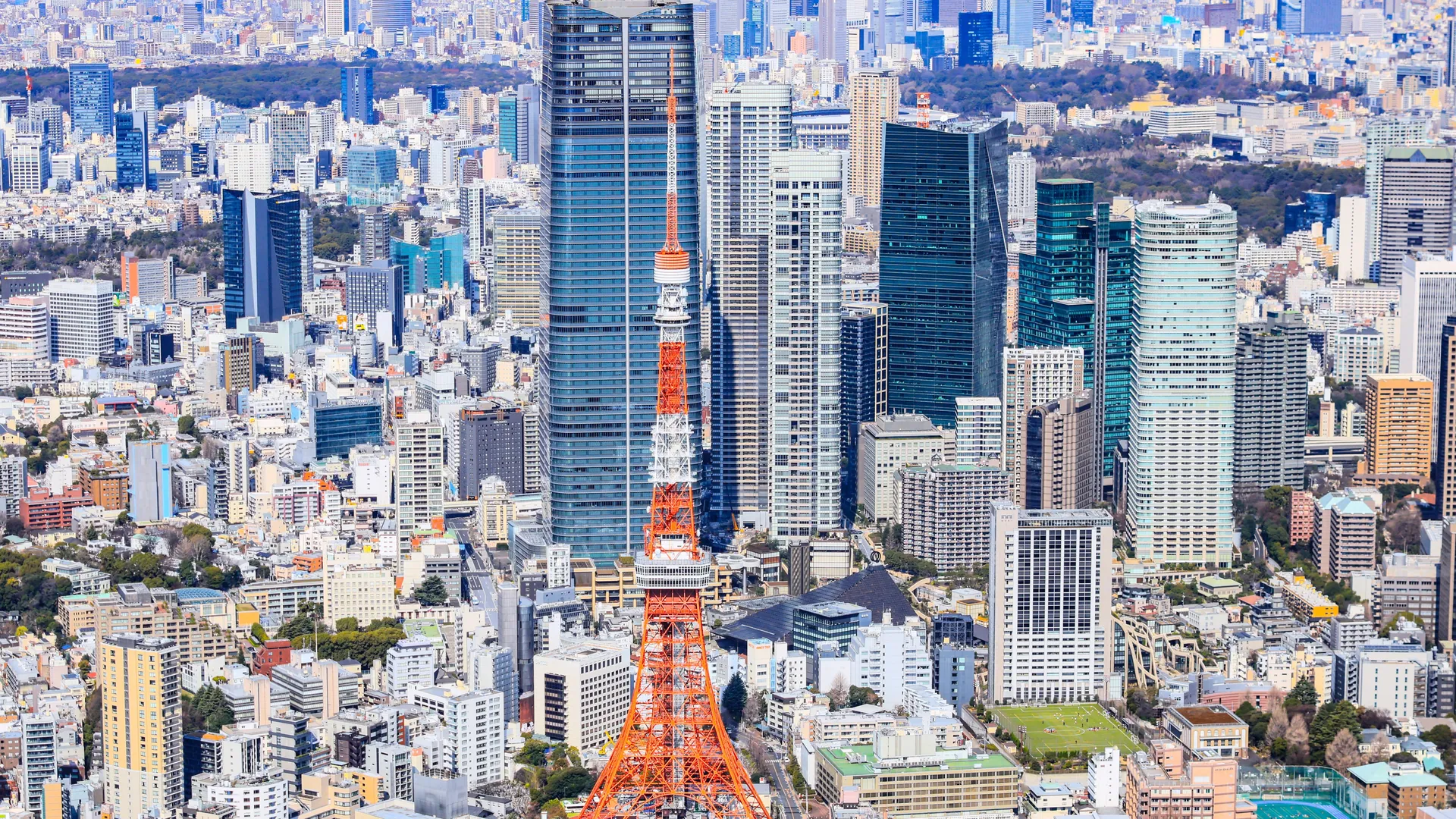 Tokyo Tower in red and white among the office towers of Minato by day, seen from a private helicopter over Tokyo
