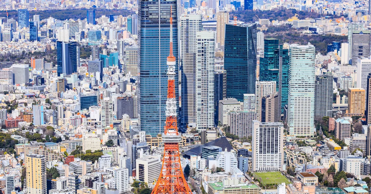 Tokyo Tower in red and white among the office towers of Minato, seen by day from a private helicopter over Tokyo