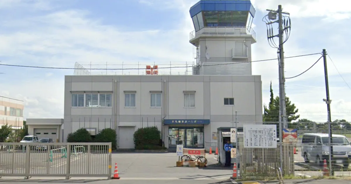A low heliport terminal building with a control tower on top and a gated entrance, on a sunny day